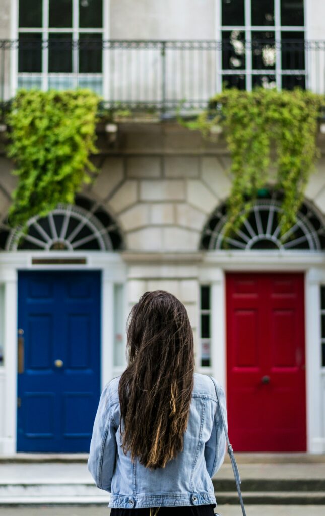 a woman stands center image facing a choice between a red door an a blue door