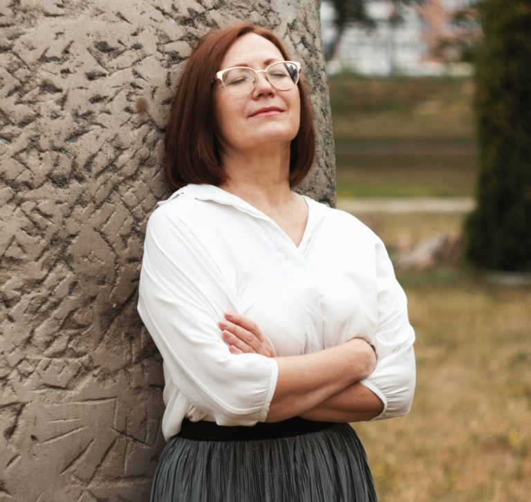 a woman leaning back on a large boulder, eyes closed, arms crossed at the front, taking a purposeful pause